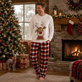 Man in matching Christmas pajamas with reindeer print top and plaid pants by a fireplace - view 2