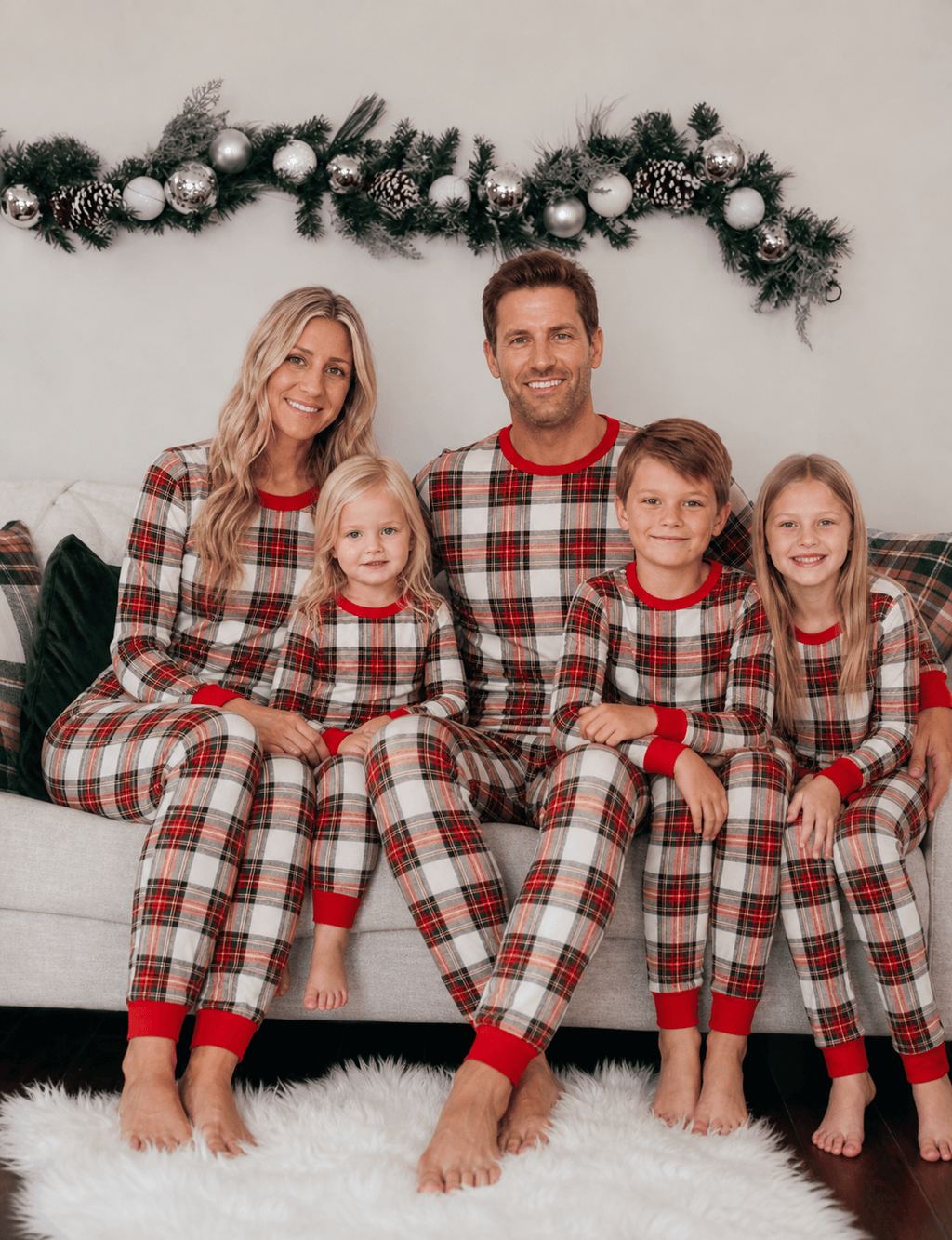 Family wearing matching cream and red tartan Christmas pyjamas with red ribbed cuffs
