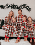 Family wearing matching cream and red tartan Christmas pyjamas with red ribbed cuffs